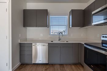 an empty kitchen with gray cabinets and stainless steel appliances and a window at Sagecrest Apartments, Washington, 98801